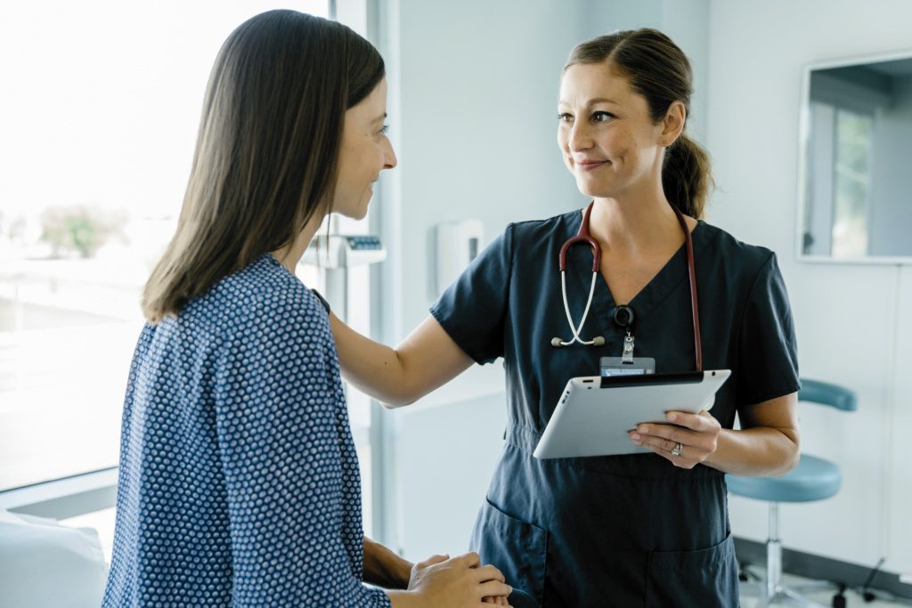 Female doctor consoling woman while holding tablet computer in medical examination room